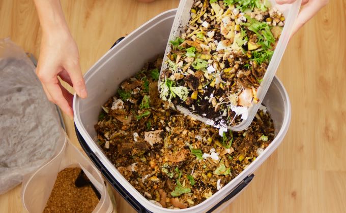 Remplissage du seau de compost bokashi avec des déchets de cuisine coupés en petits morceaux.