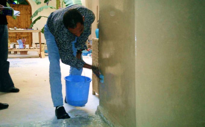 Artisan marocain entretenant un mur enduit au tadelakt avec du savon noir.